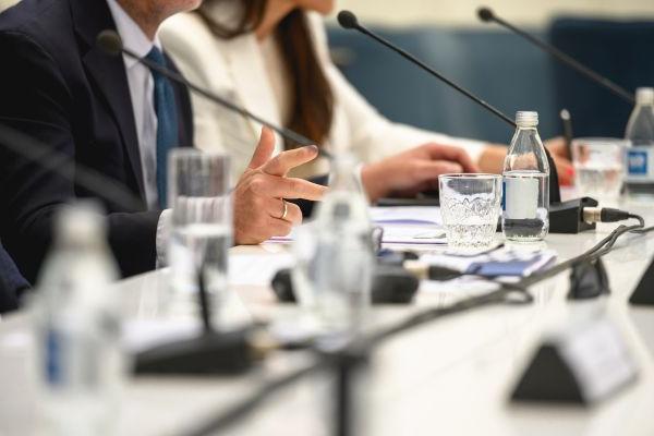 Woman and man at press table with microphones and name cards.